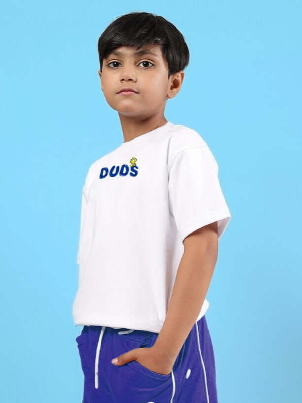 Boy wearing DUDS oversized white T-shirt with blue shorts against a blue background.