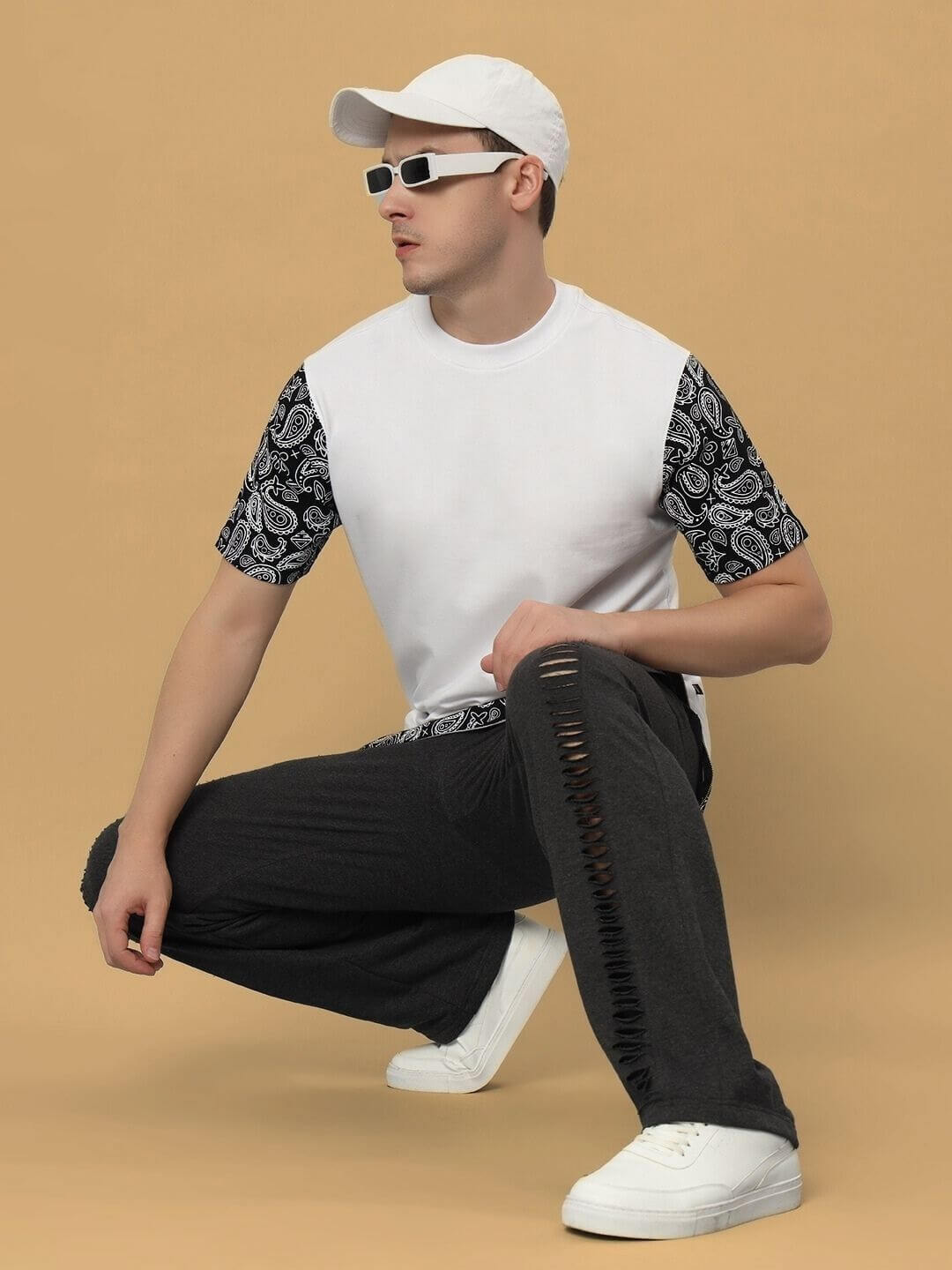Model wearing Beasley Over-Sized T-Shirt in white with black patterned sleeves, paired with ripped jeans and white sneakers against a beige background.