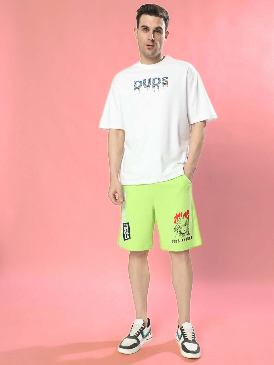 Man wearing MELTING EARTH OVER-SIZED T-SHIRT WHITE with graphic design, styled with neon green shorts on a pink background.