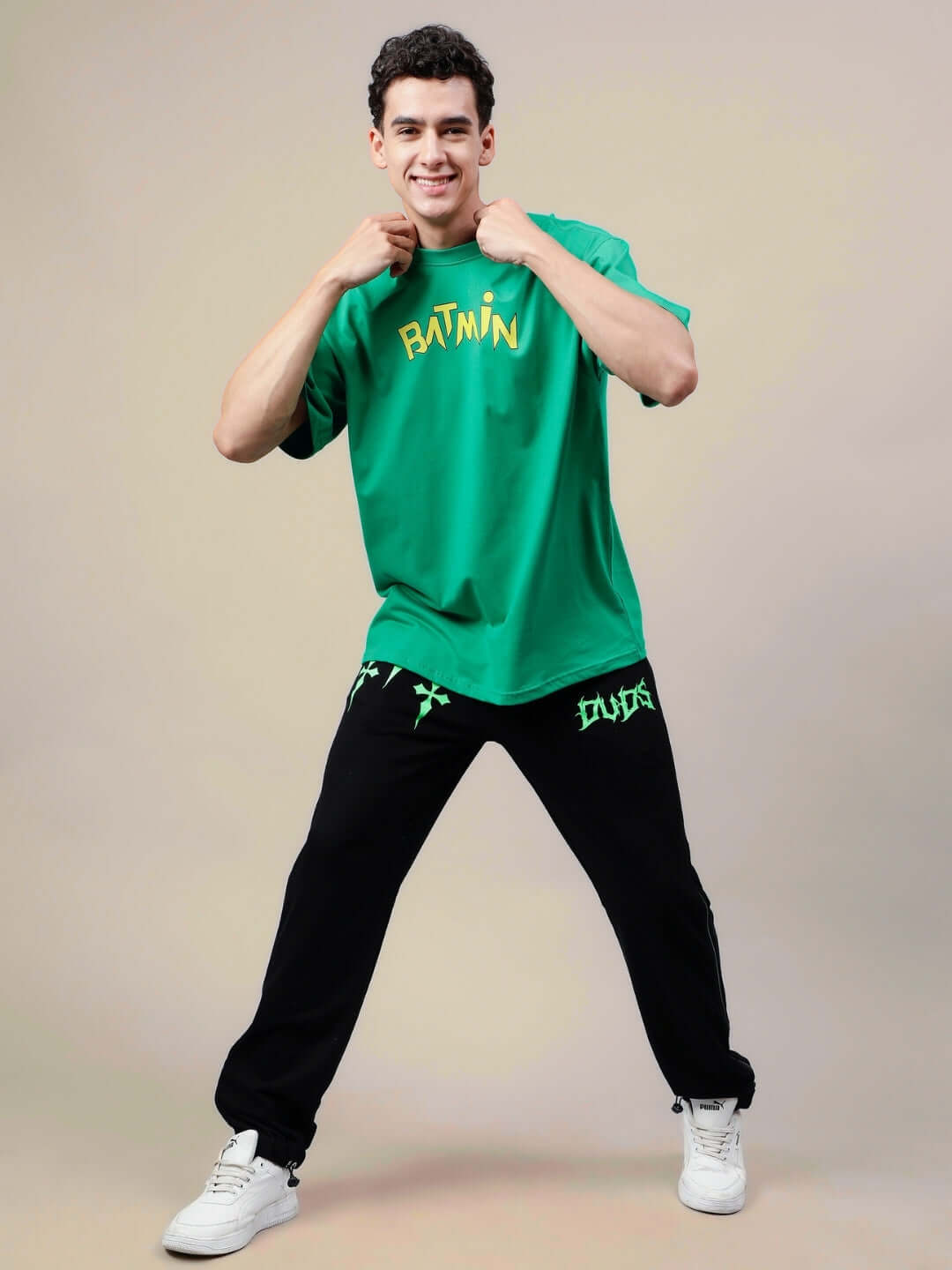 Man wearing BATMIN OVER-SIZED T-SHIRT GREEN, standing confidently in casual black pants and white sneakers.