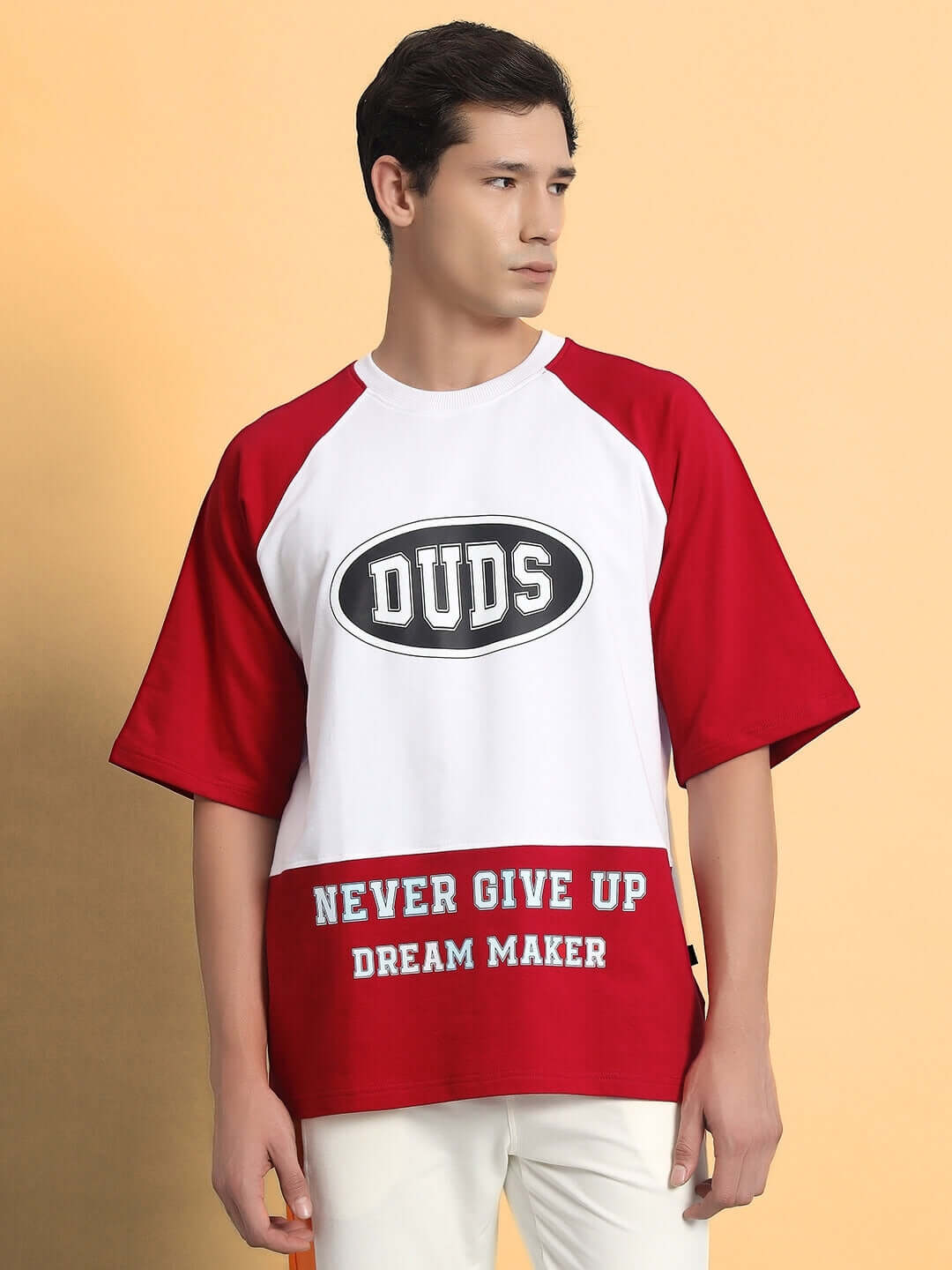 Man wearing a red and white NEVER GIVE UP OVERSIZED T-SHIRT RED with "DUDS" and "DREAM MAKER" text.