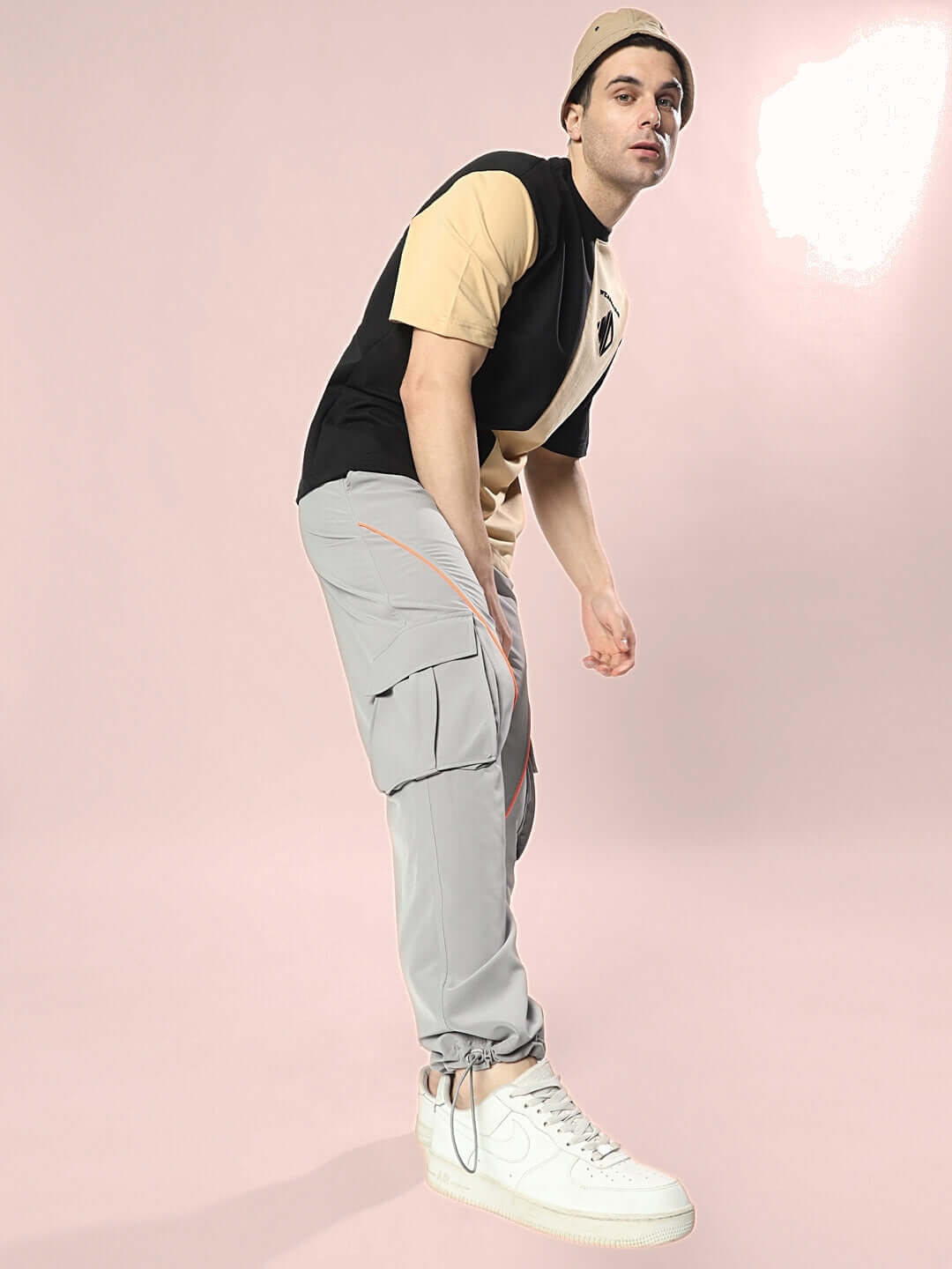 Model wearing DRAGON OVERSIZED T-SHIRT BLACK BEIGE with casual gray pants and white sneakers, posed on a pink background.