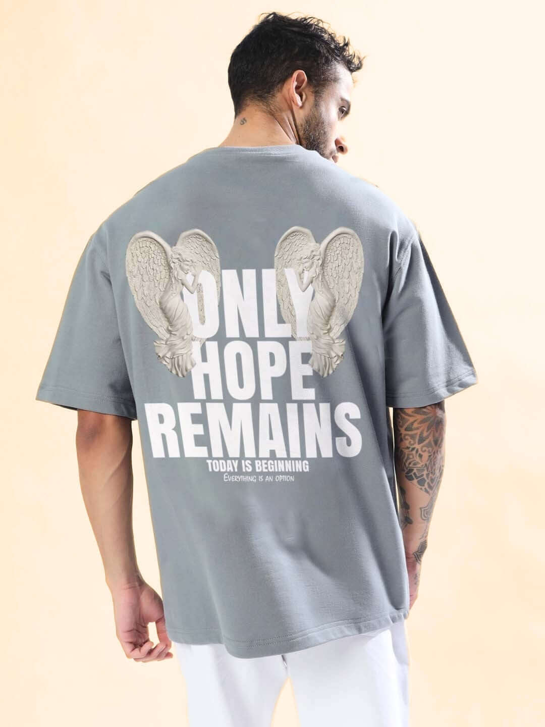 Model wearing ONLY HOPE REMAINS OVER-SIZED T-SHIRT GREY with bold graphic print on the back, highlighting contemporary streetwear style.