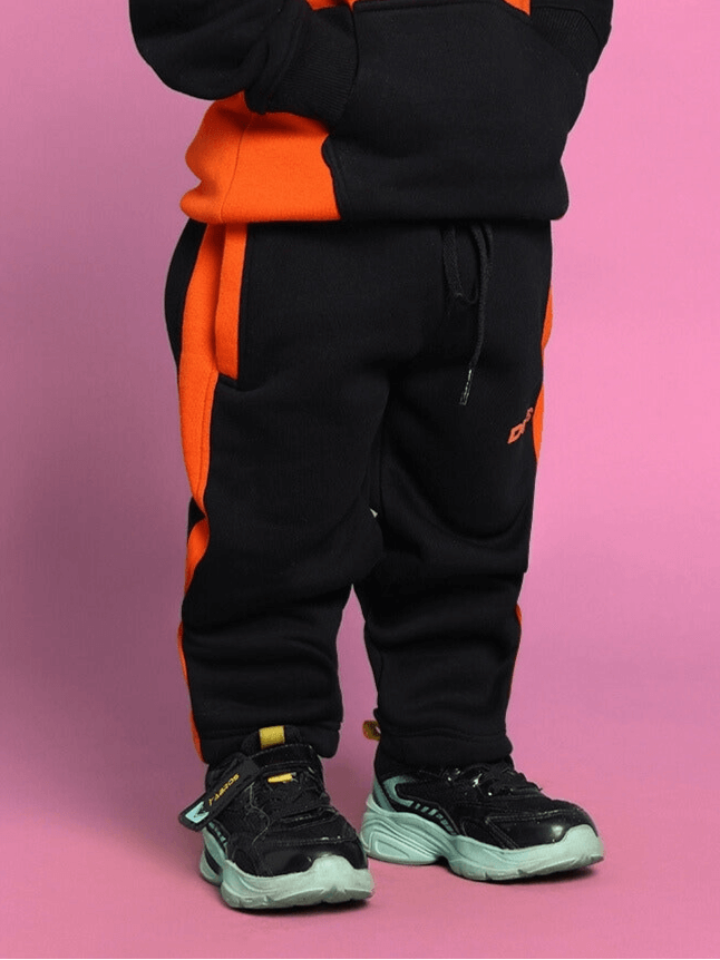 Child wearing black-orange COOL TEDDY co-ord set with oversized fit and modern design for boys and girls, standing against pink background.