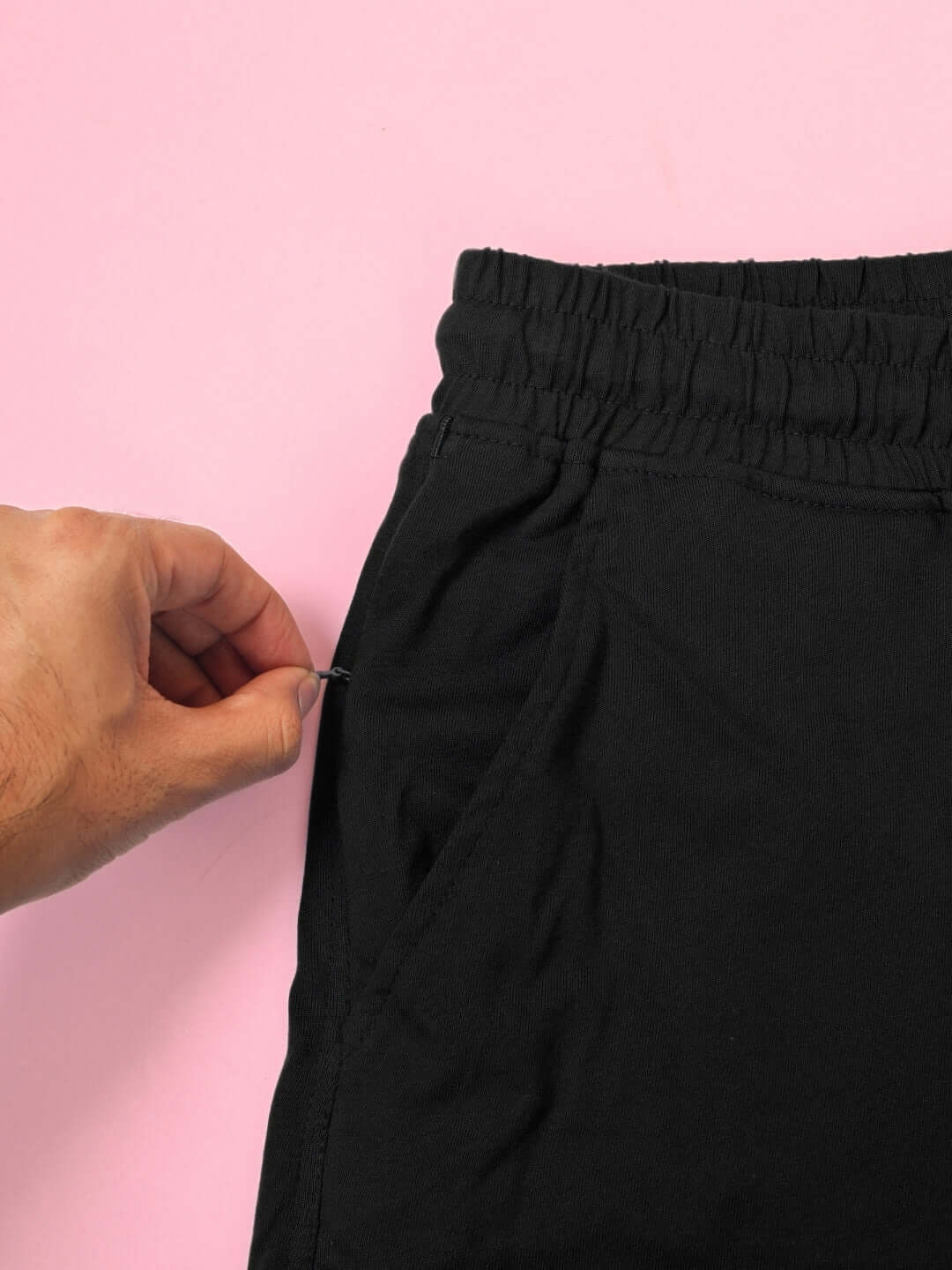 Close-up of black pants with an elastic waistband and pockets, highlighting the premium cotton French terry fabric on a pink background.