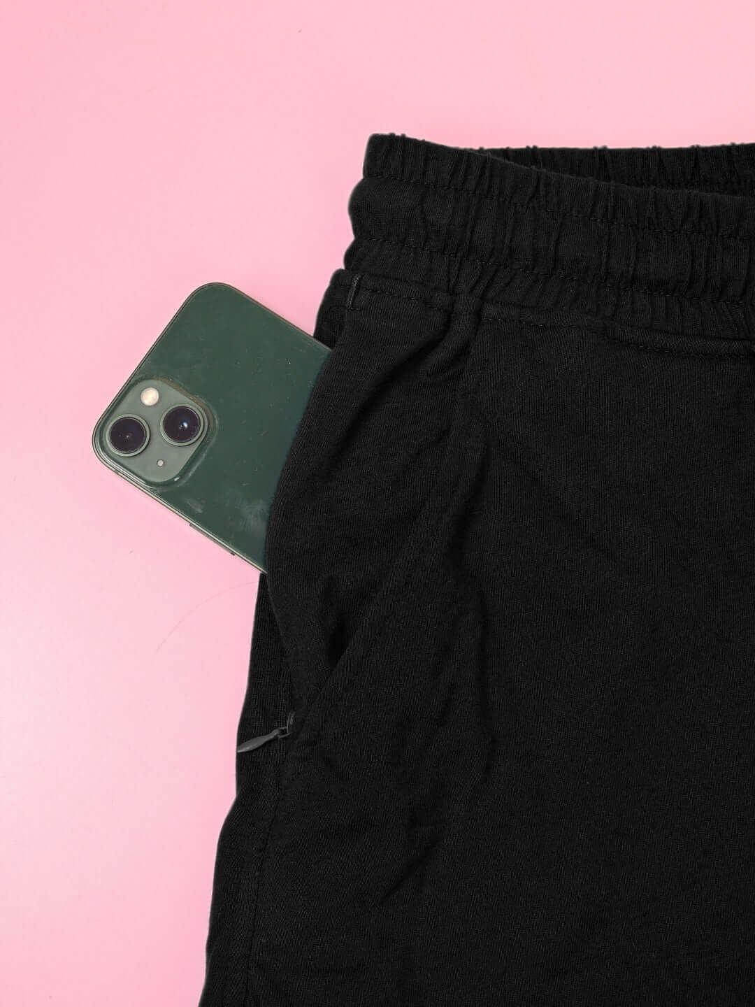 Black co-ord set pants pocket holding a green smartphone against a pink background.
