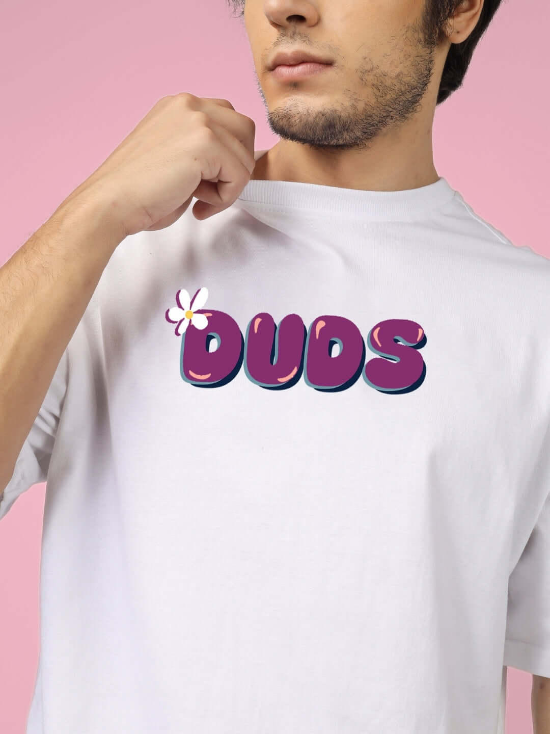 Close-up of a person wearing a white t-shirt with 'Duds' in bold purple text and a flower design on a pink background.