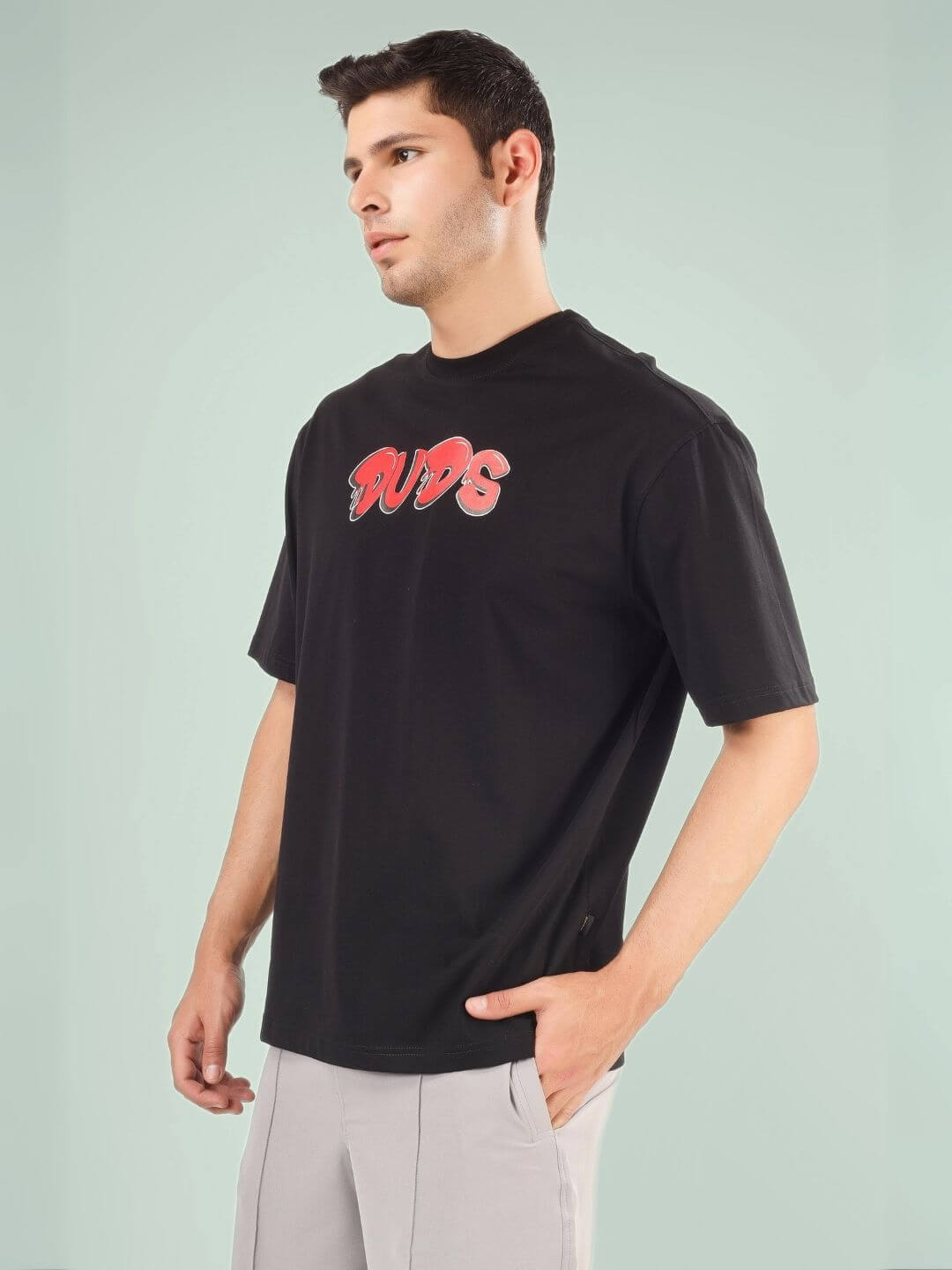 Model wearing DRIP 2 HARD OVER-SIZED T-SHIRT BLACK by DUDS, side view, casual fashion style.