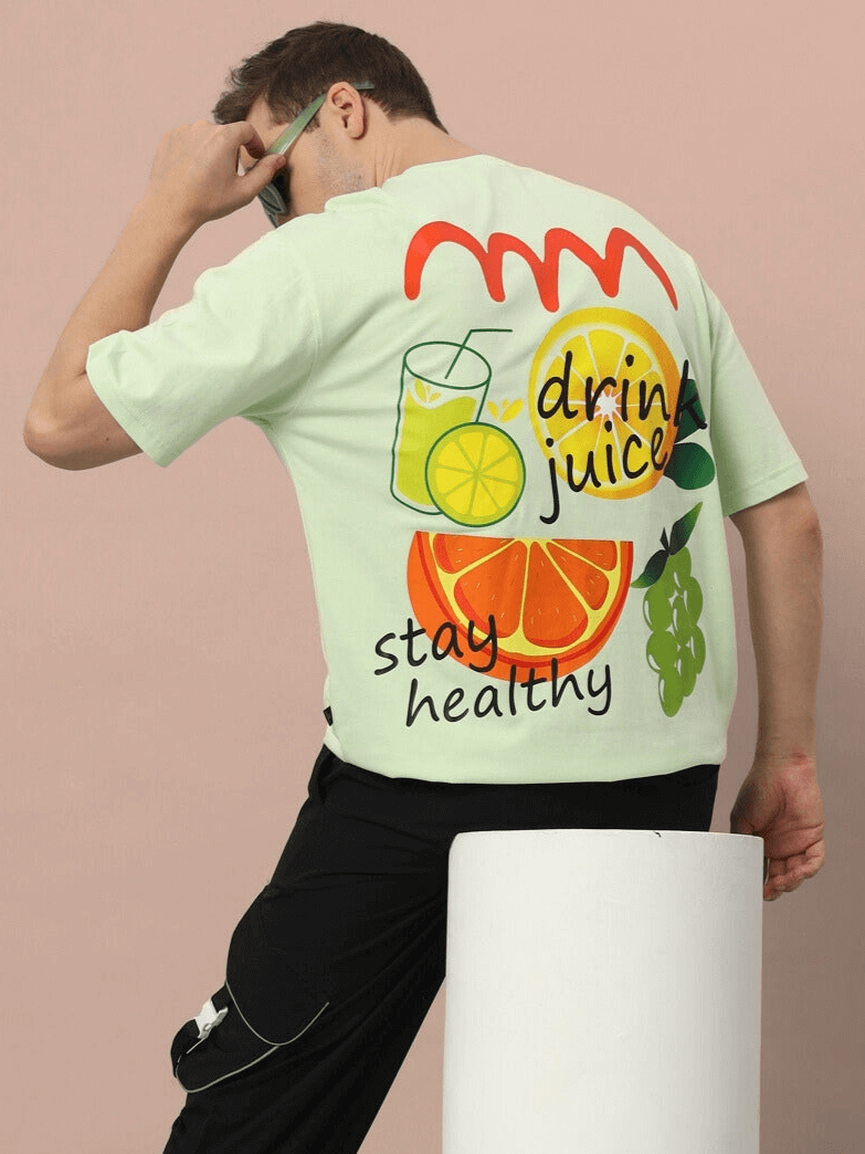 Person wearing DRINK JUICE OVER-SIZED T-SHIRT CELERY ICE with fruit graphics and text "stay healthy."