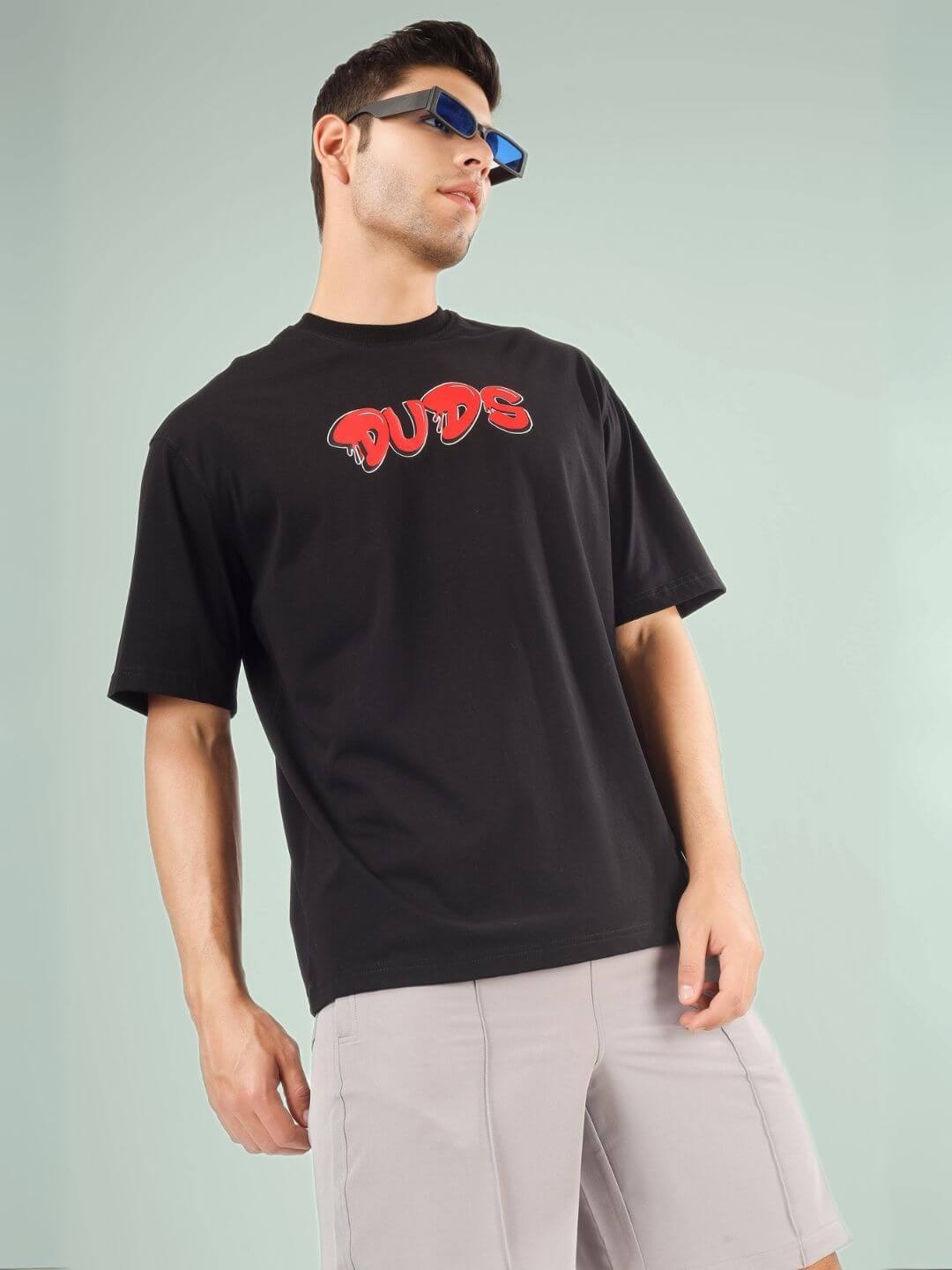 Model wearing DRIP 2 HARD OVER-SIZED T-SHIRT BLACK with DUDS logo and sunglasses.