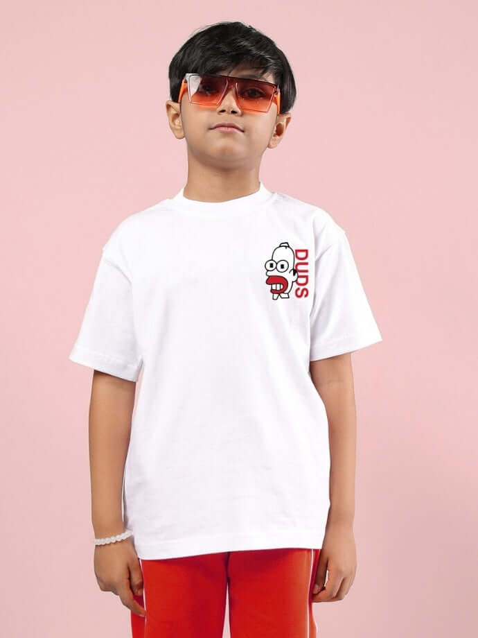 Child wearing white Simpsons oversized T-shirt with cartoon graphic, red pants, and red sunglasses against pink background.
