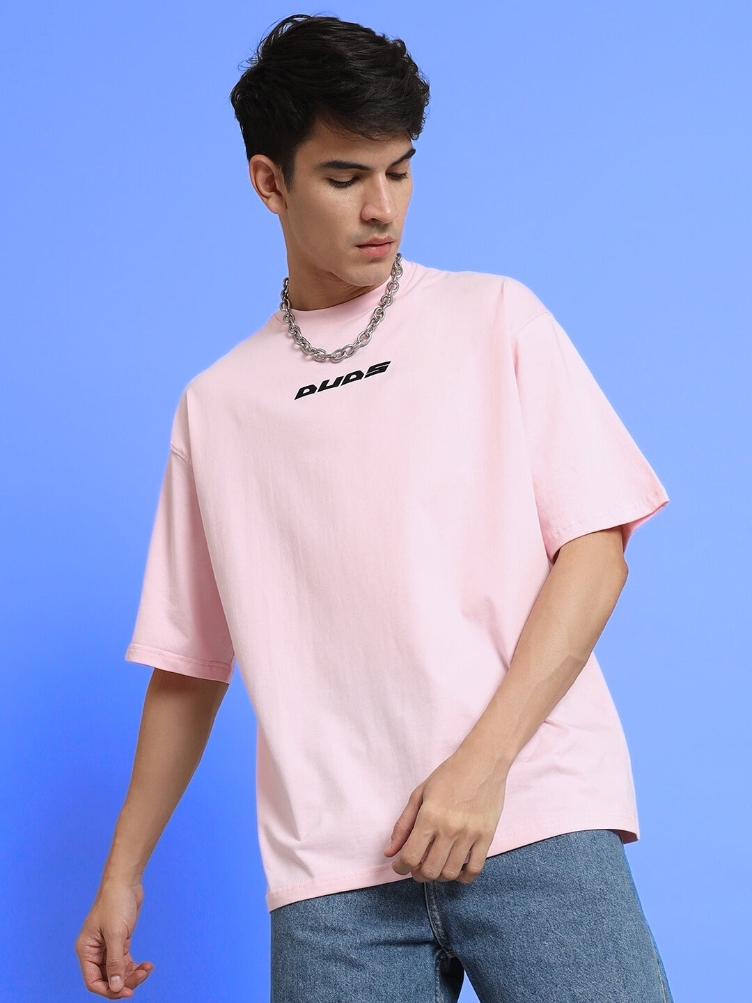 Model wearing pink TOP-DOG oversized t-shirt with DUDS logo, available in customizable sizes and custom fit option on blue background.