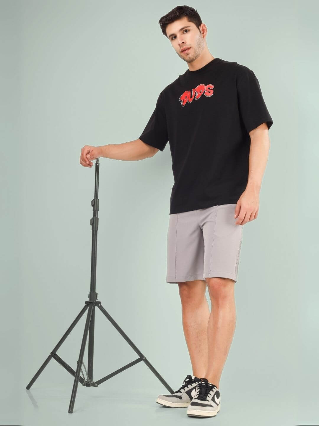 Model wearing DRIP 2 HARD OVER-SIZED T-SHIRT BLACK posing with tripod in studio