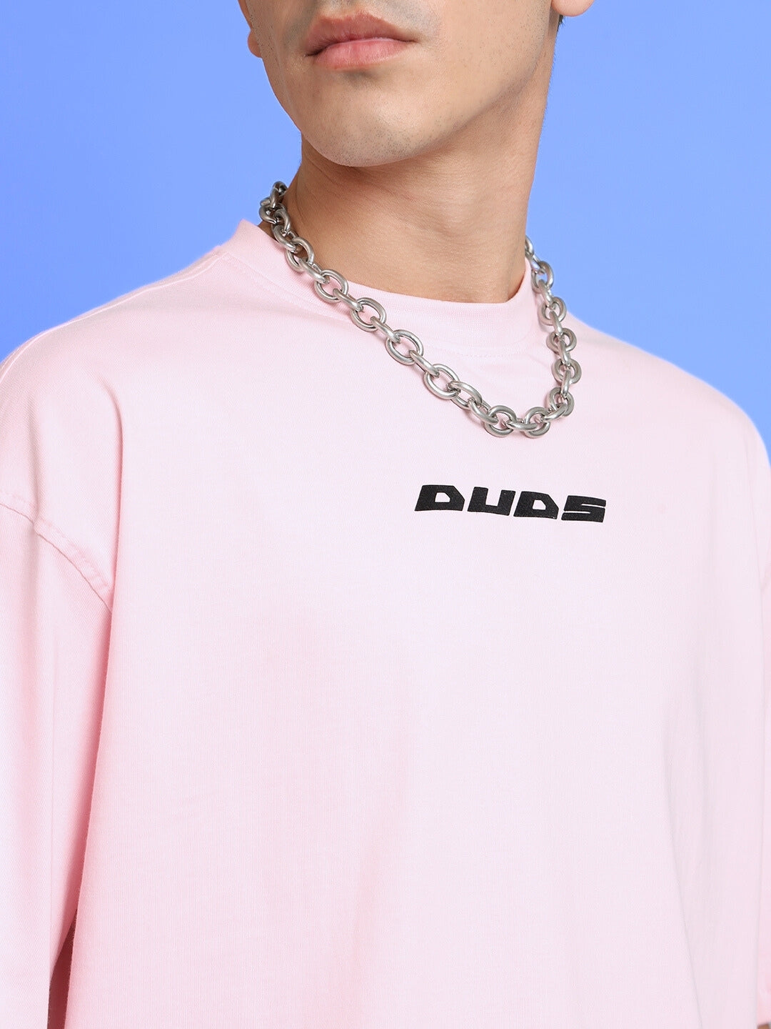 Person wearing pink oversized DUDS T-shirt and a chunky silver necklace, close-up view.