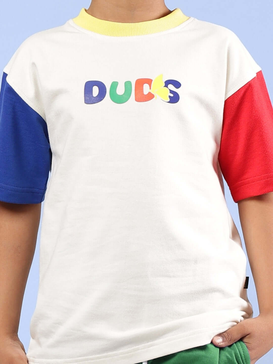 Child wearing ADONIS co-ord set with off-white top featuring colorful DUDS logo, complemented by red and blue sleeves.
