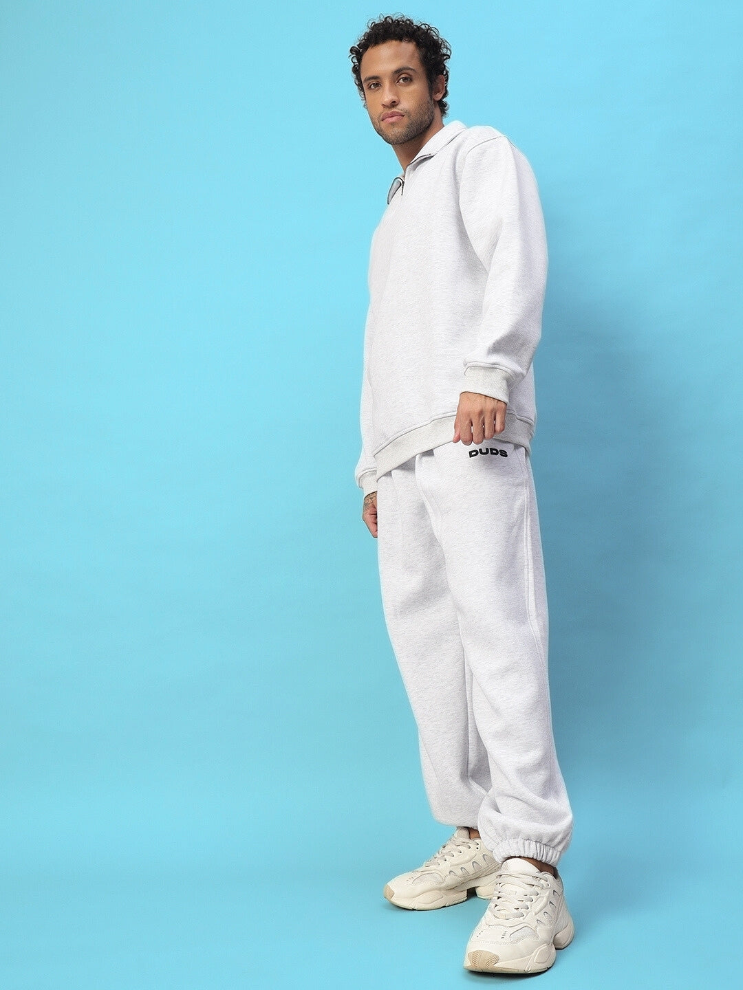 Man wearing Bona-Fide Fleece Pant in melange grey with matching sweatshirt, standing against a blue background.