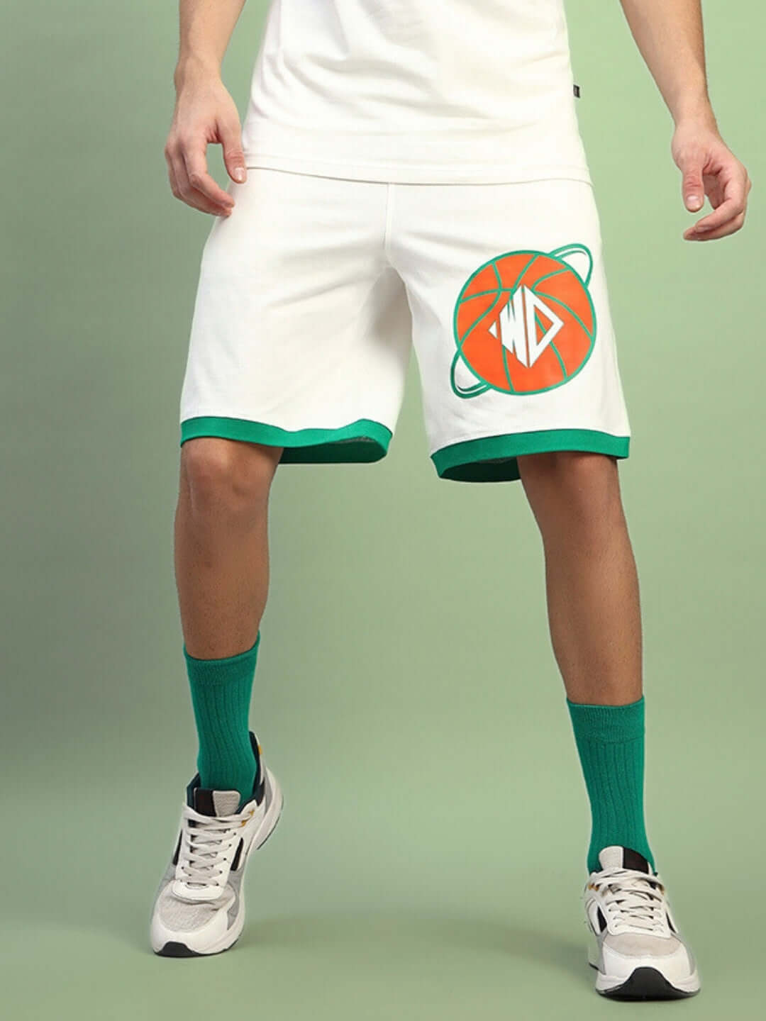 Man wearing off-white Dribble Summer Shorts with green trim and graphic, paired with green socks and running shoes, against a green backdrop.