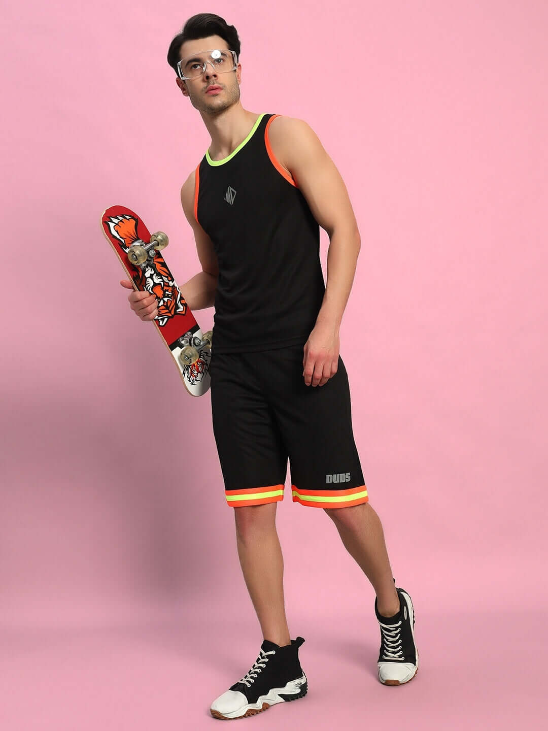 Man wearing black Jordan gym co-ord set holding skateboard, against pink background. Sports polyester, cold machine wash. Made in India.