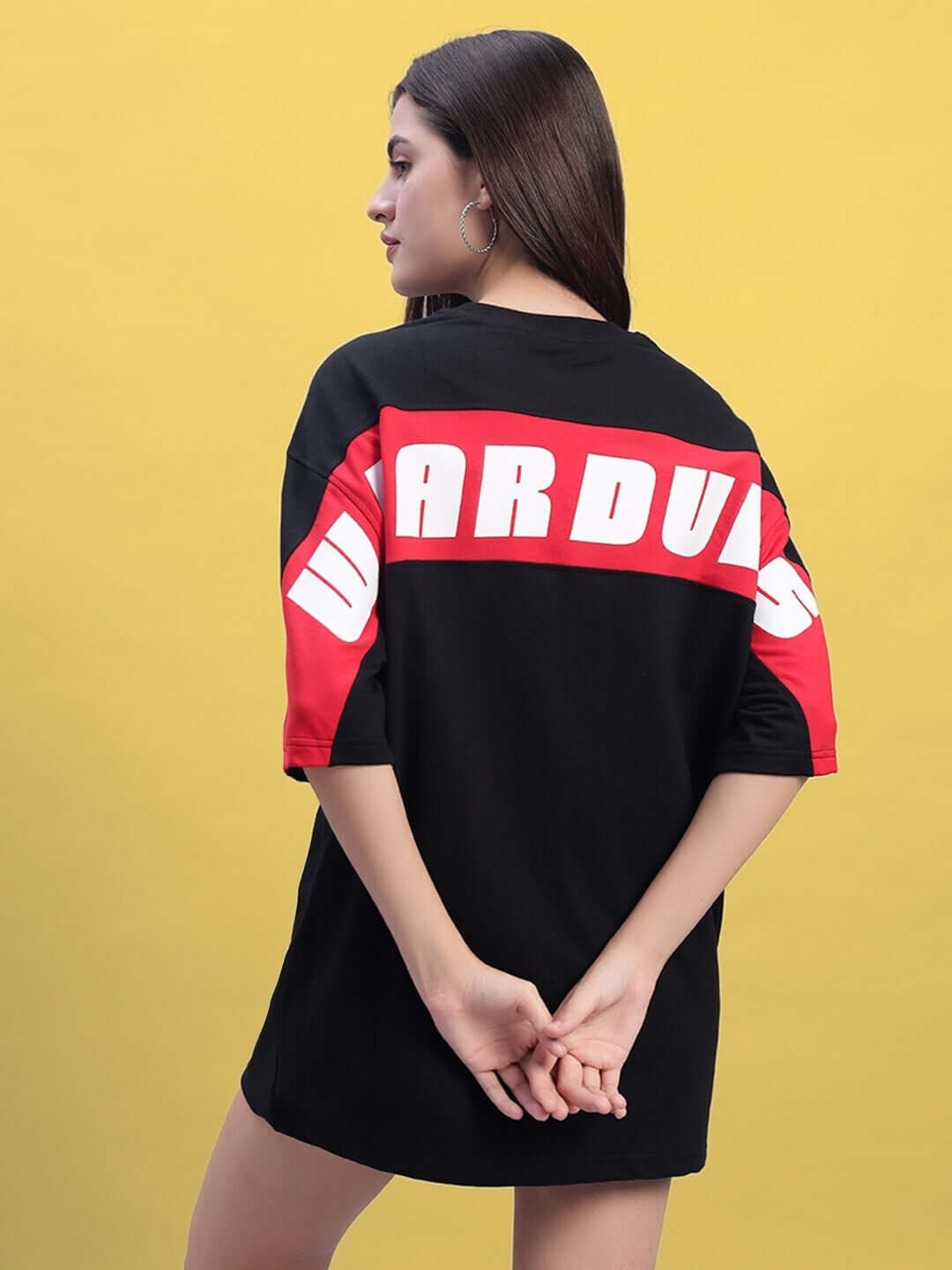 Model wearing a women's oversized black and red Titan T-shirt with bold lettering, showcasing the back design against a yellow background.