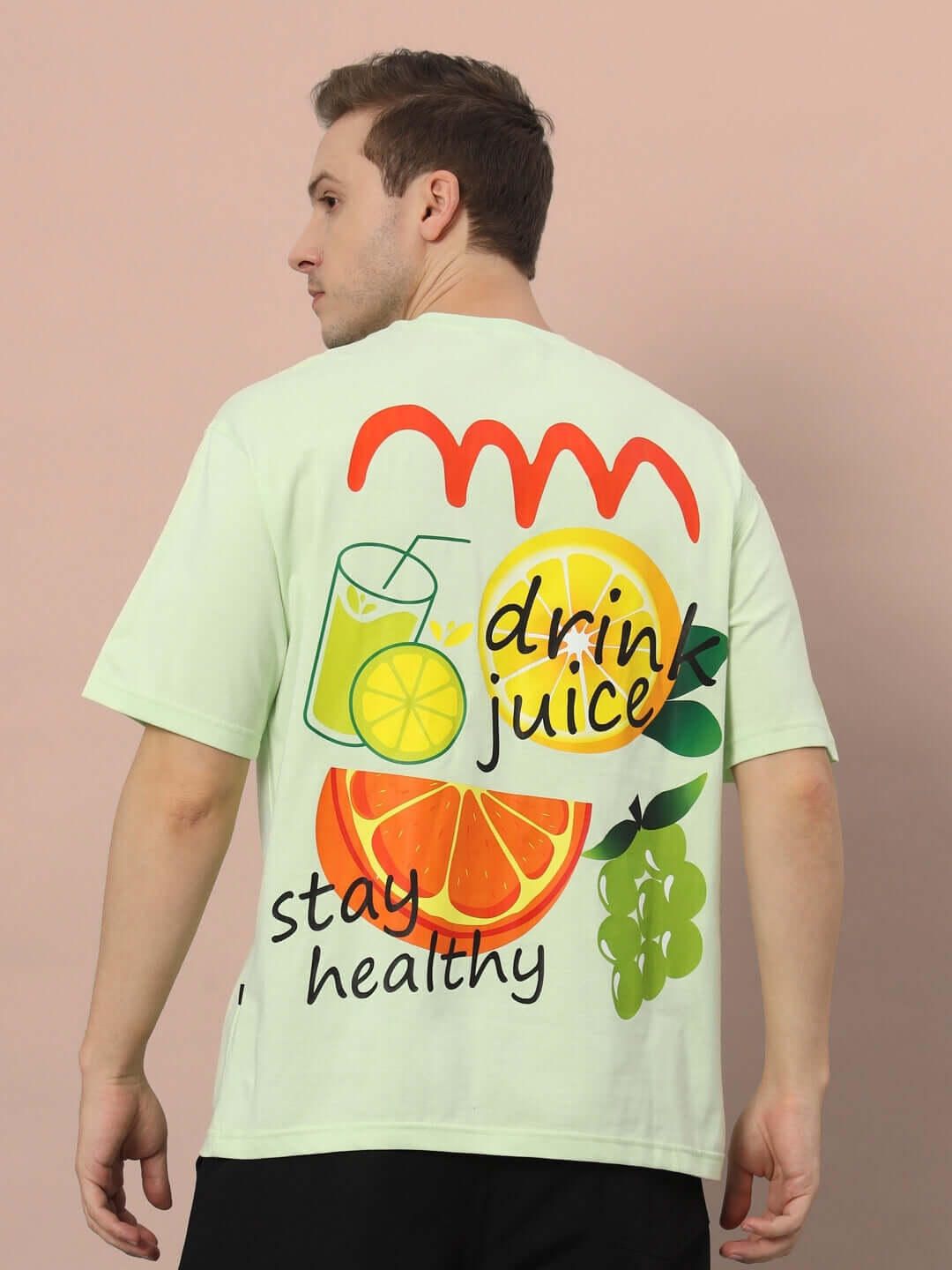 Man wearing DRINK JUICE OVER-SIZED T-SHIRT CELERY ICE with colorful fruit graphics, back view.