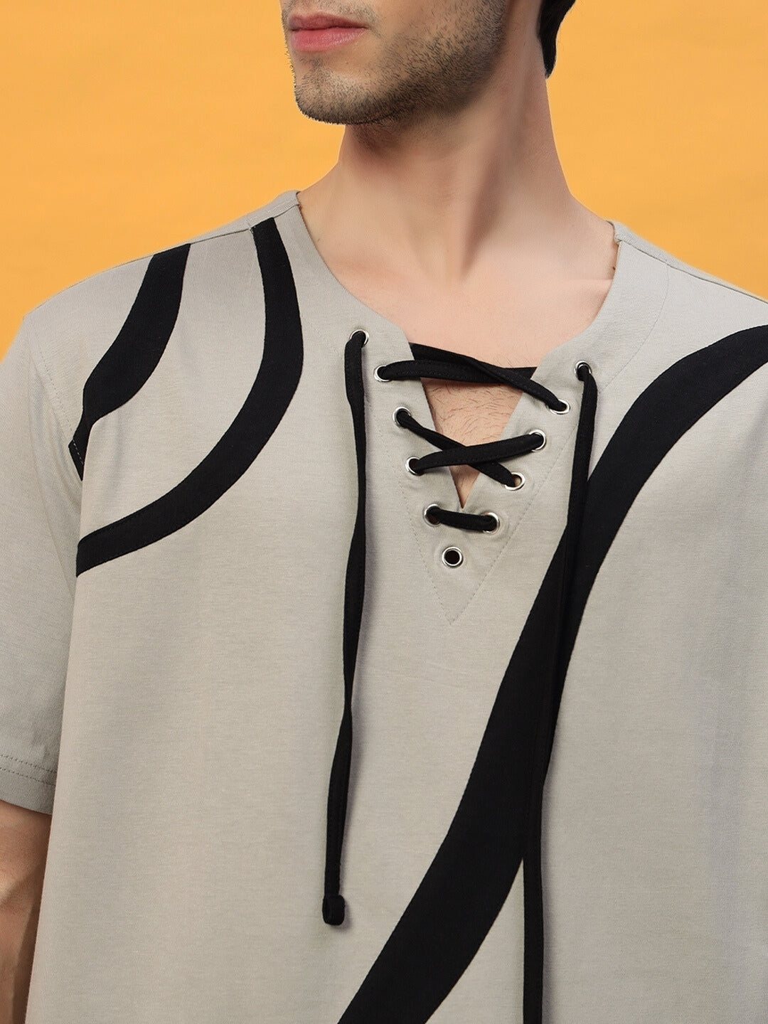 Close-up of grey designer oversized T-shirt with black abstract design and lace-up neckline, featuring premium cotton fabric.