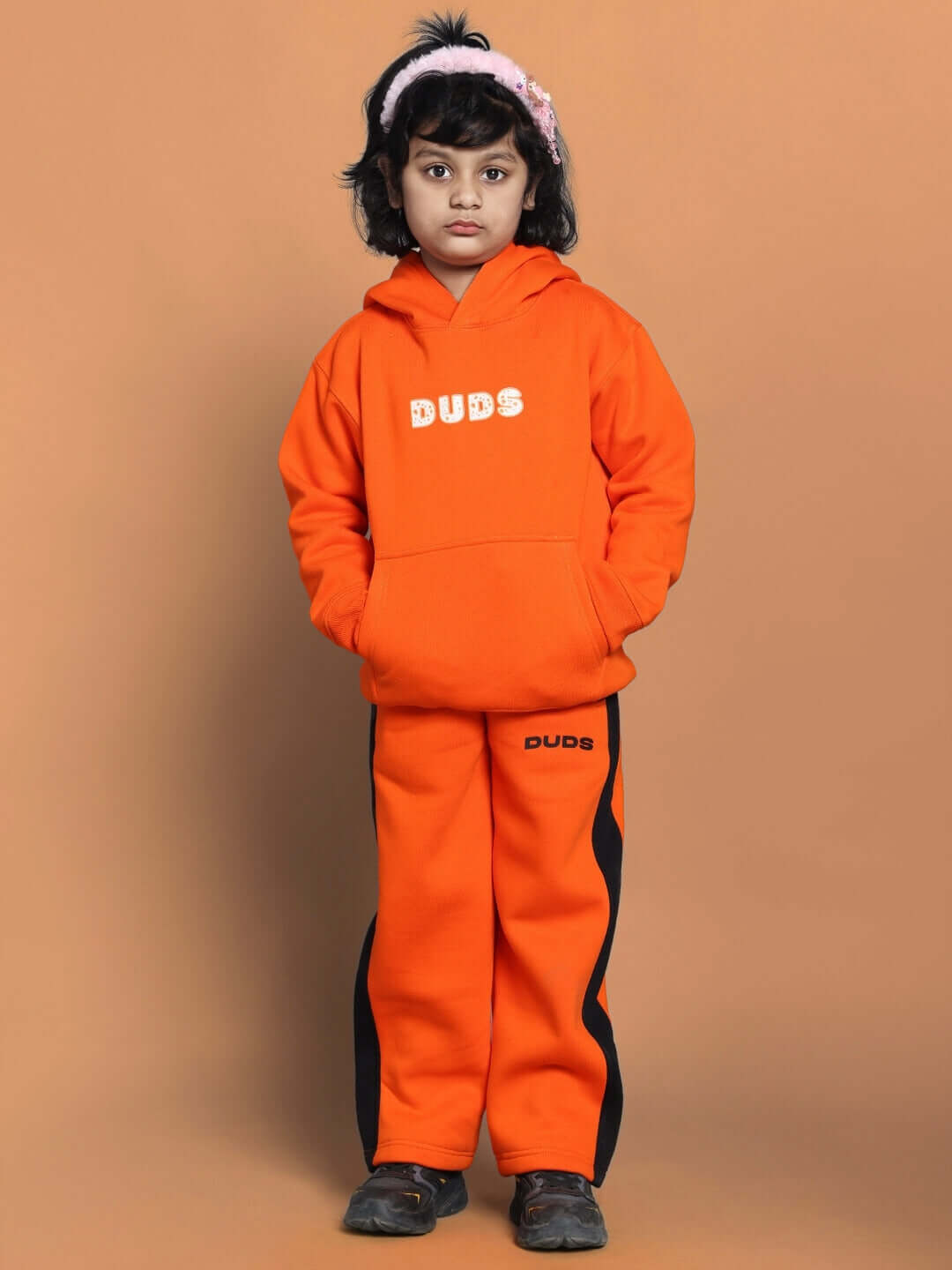 Child wearing orange "Courage Fleece Pant" and hoodie by Duds, showcasing cozy and energetic kids' fashion.