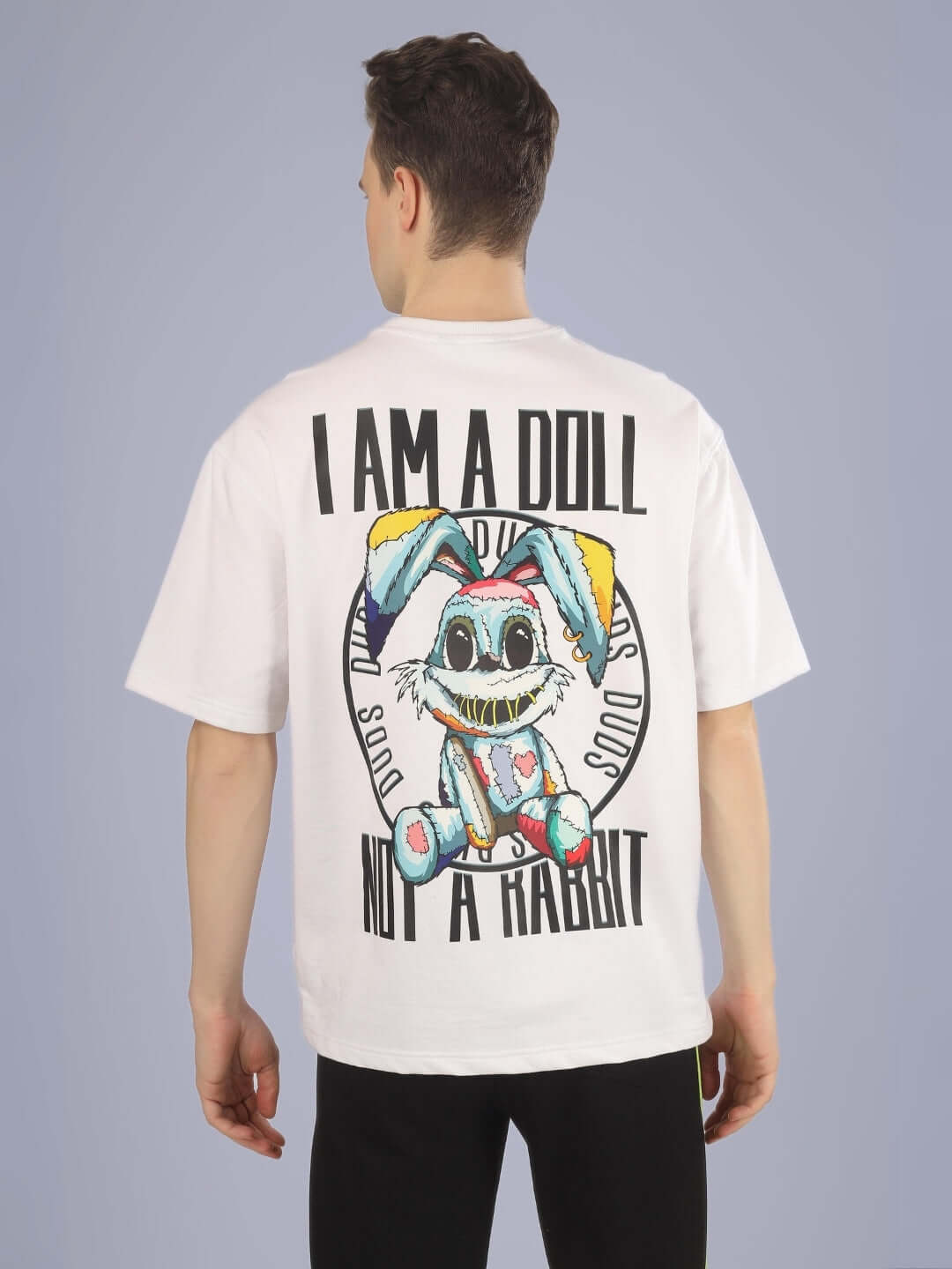 Back view of a white oversized t-shirt with colorful printed design saying 'I Am A Doll Not A Rabbit', worn by a person.