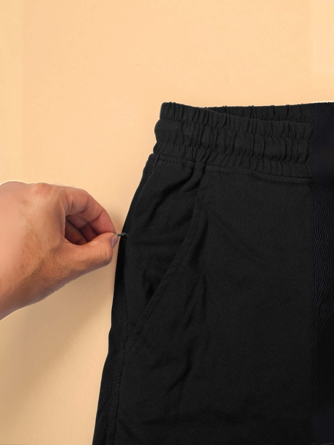 Close-up of a hand adjusting the pocket of black pants, featuring an elastic waistband, crafted from premium cotton fabric.