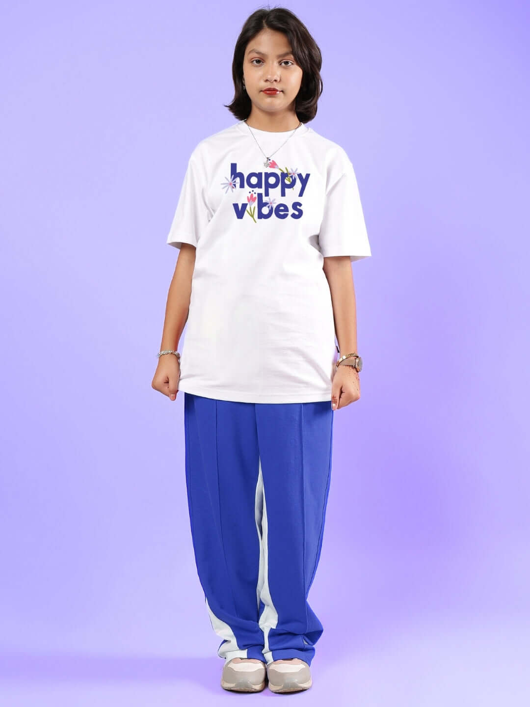 Child wearing a white Happy Vibes T-shirt and blue pants, standing against a purple background.