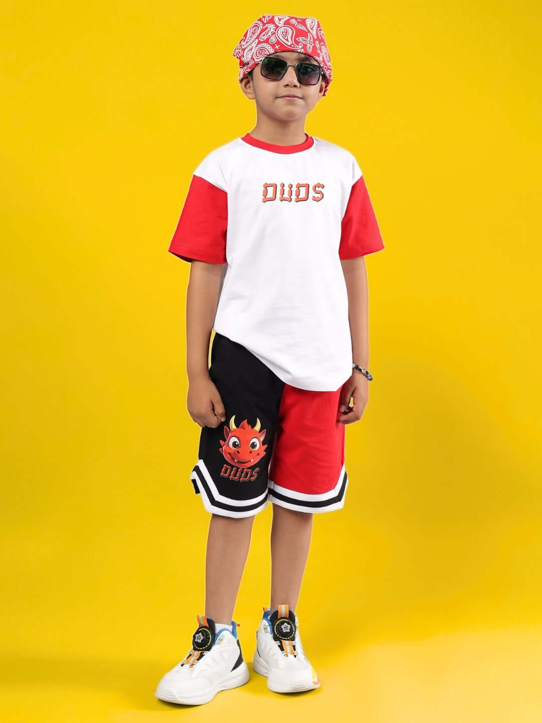 Child wearing white-red Cassie T-shirt, standing confidently in sunglasses against yellow background. Unisex, customizable fit by DUDS.