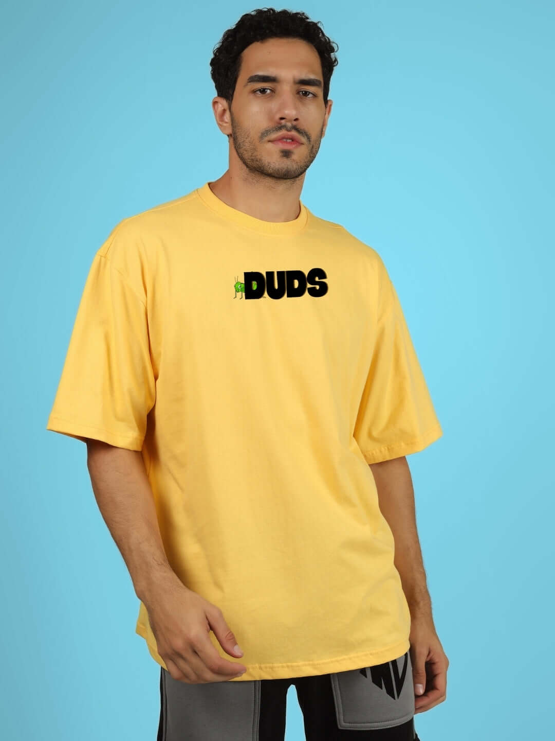 LOCUST OVER-SIZED T-SHIRT YELLOW worn by model against blue background, featuring DUDS logo