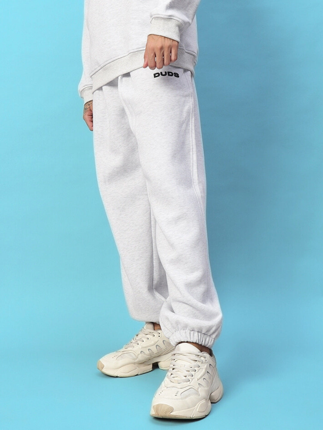 Person wearing Bona-Fide Fleece Pant in Melange Grey with casual sneakers on blue background.