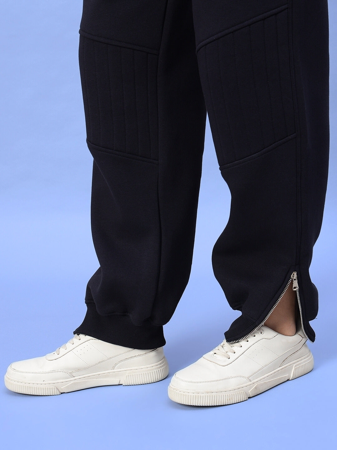 Close-up of navy blue women's Fight Night fleece co-ord pants with side zippers, paired with white sneakers against a light blue background.