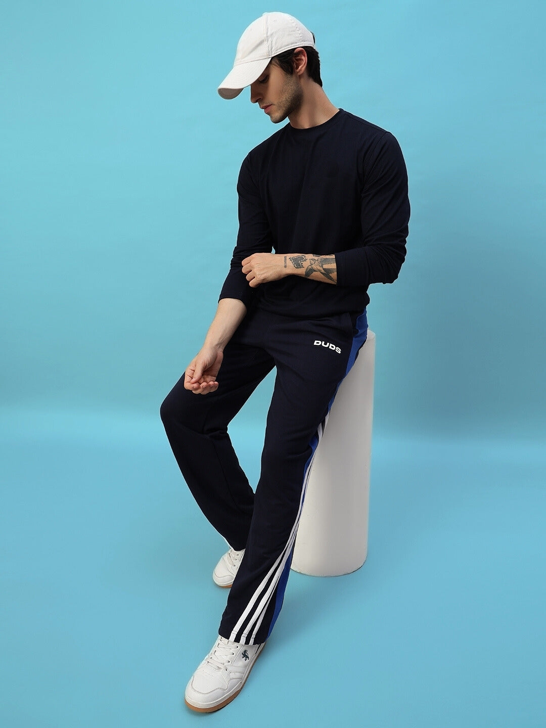 Model wearing TANGLE Relaxed-Fit Joggers in navy blue by DUDS, seated with casual style against blue background.