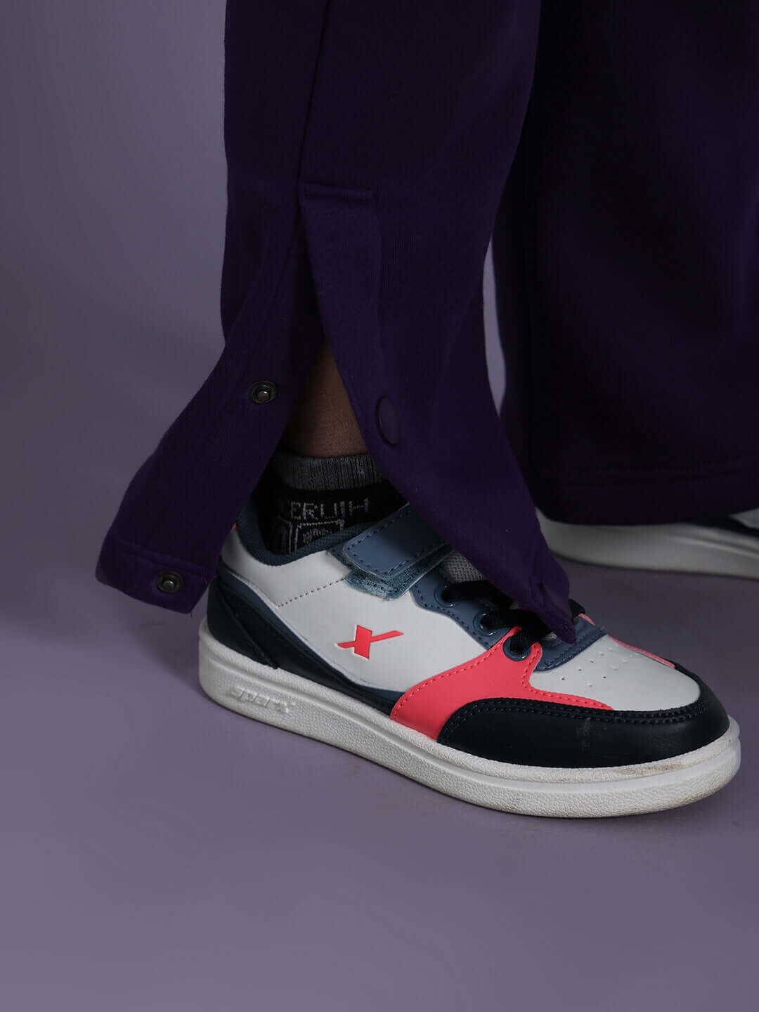 Close-up of feet wearing white sneakers with red and black accents, paired with purple pants showcasing the Miller Co-ord fashion outfit.