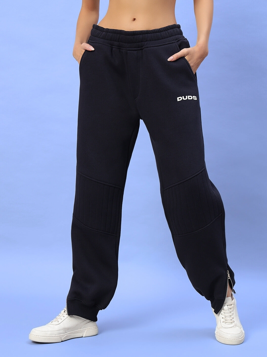 Navy blue workout pants for women with elastic waistband and logo design, paired with white sneakers on a light blue background.