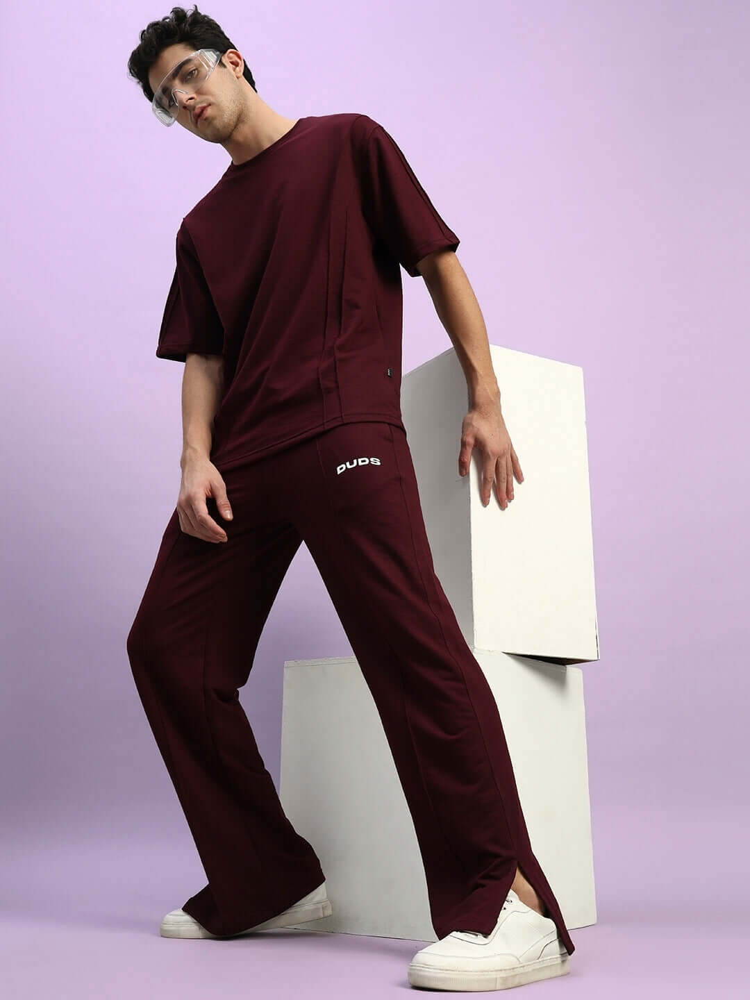 Model wearing ZION Relaxed Fit Co-Ord Set in maroon with elasticated waistband, 97% cotton, unisex design against a purple backdrop.
