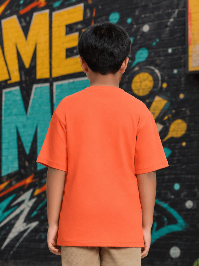 Boy wearing a COMIC STREET T-SHIRT FOR BOYS GIRLS ORANGE standing against a colorful graffiti wall.
