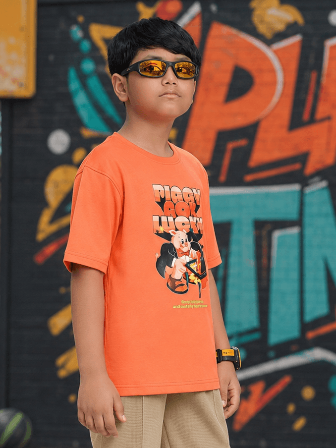Boy wearing a COMIC STREET T-SHIRT FOR BOYS GIRLS ORANGE with a cool graphic, sunglasses, against a colorful backdrop.