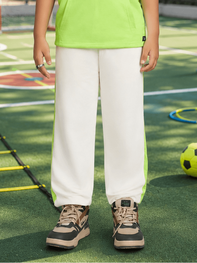 CURIOUS JOGGER FOR BOYS GIRLS OFF WHITE paired with a bright green top on a playful outdoor sports field.