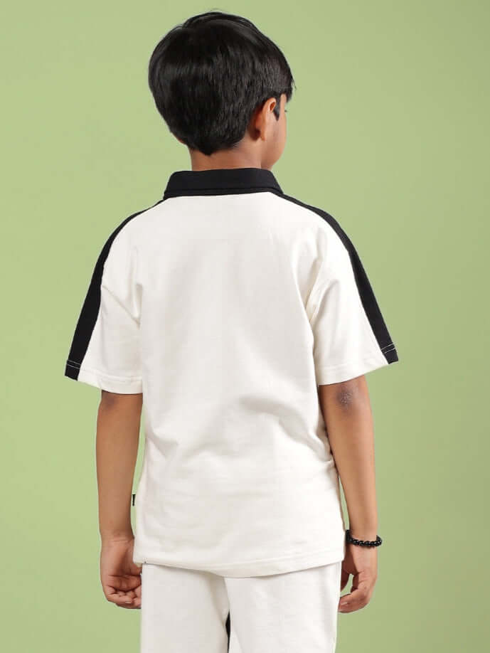 Boy wearing off-white Splinter T-shirt with black trim from DUDS, made to order for boys and girls, shown from the back view on a green backdrop.