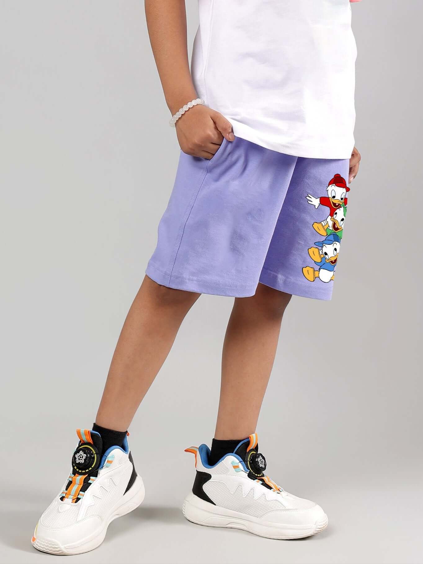 Child wearing lavender duck-themed shorts with white sneakers.