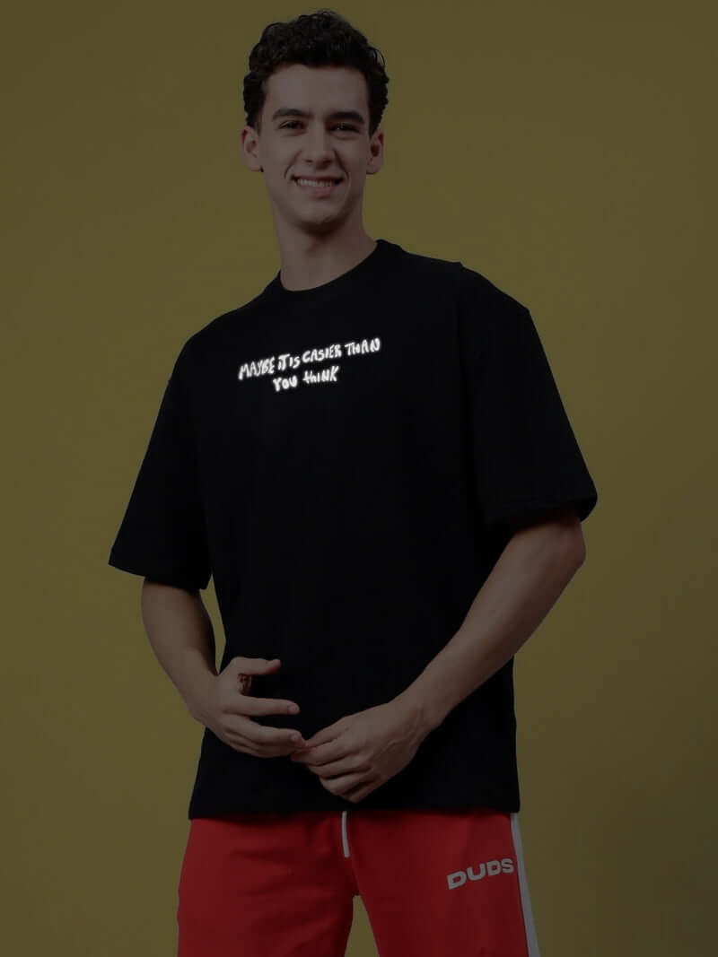 Person wearing MAYBE IT IS EASIER THAN YOU THINK REFLECTOR T-SHIRT BLACK, showcasing reflective text design.