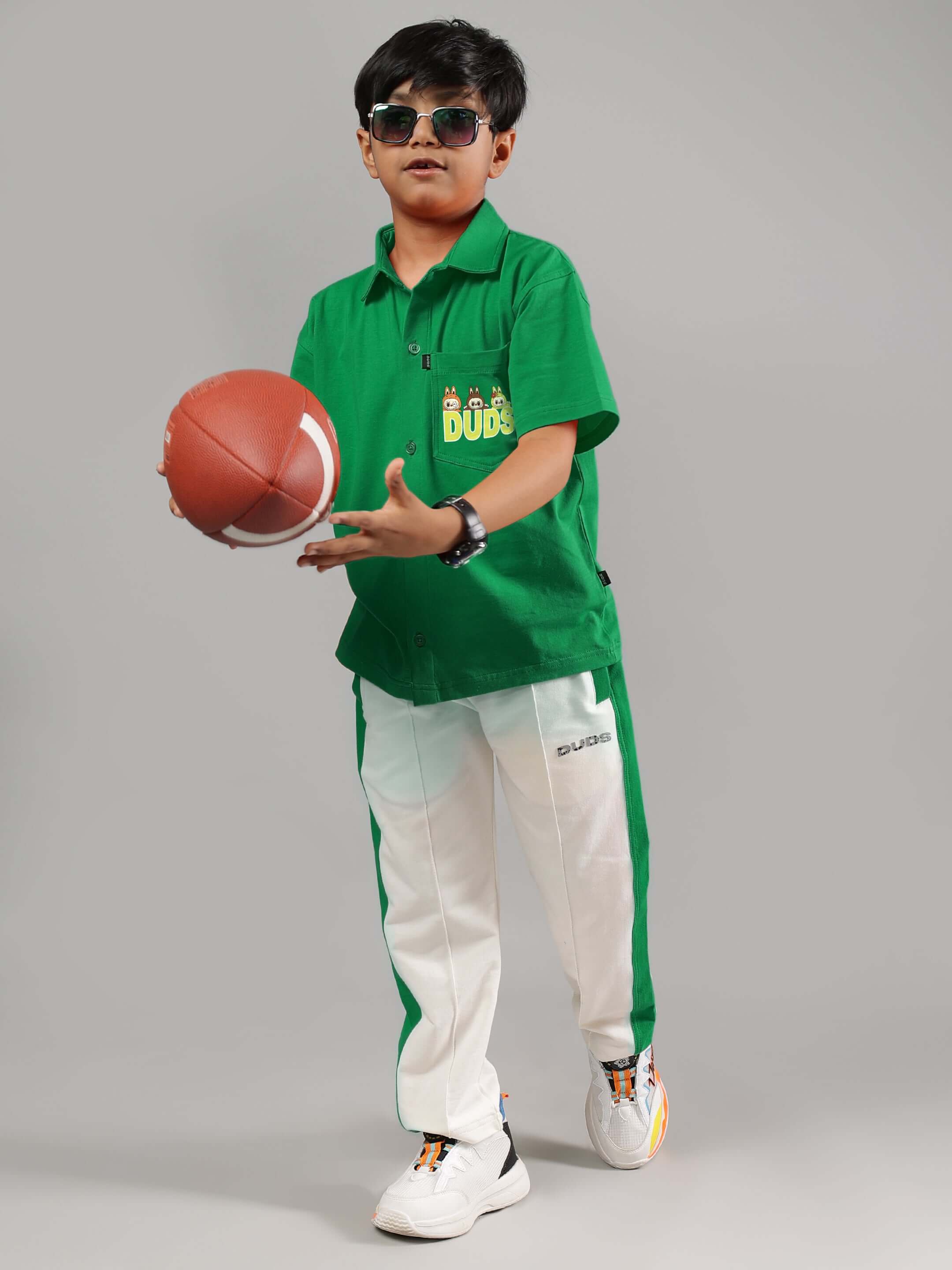 Boy wearing Labubu Mystery Co-ord Set in green and off-white, holding a football and wearing sunglasses.