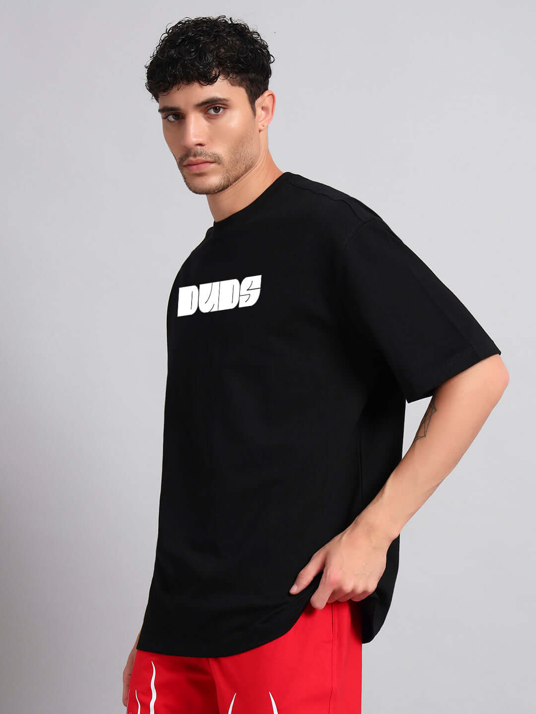 Model wearing a black oversized Guns and Roses T-shirt with bold graphic text, paired with red pants, ideal for trendy summer fashion.
