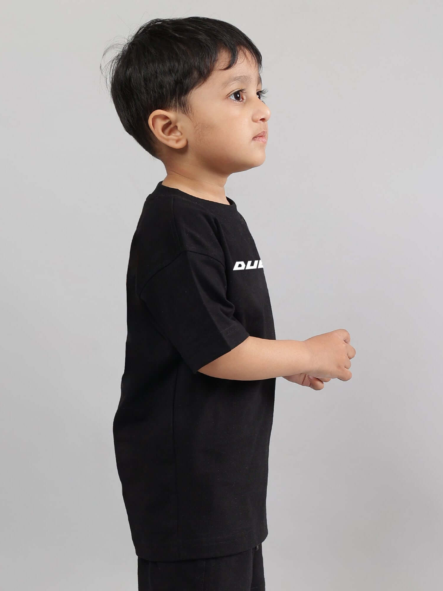 Young child wearing a black "Enjoy the Wind" T-shirt by DUDS, suitable for both boys and girls.