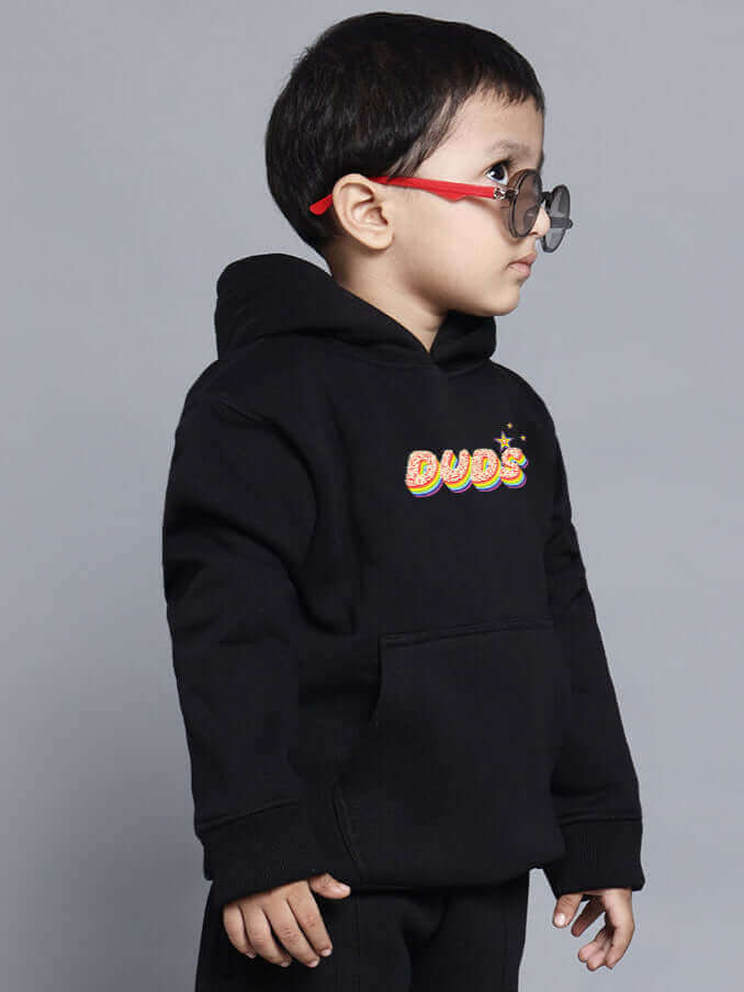Young child wearing a black "Born to Shine" co-ord set for boys and girls, featuring colorful text on the hoodie, standing in profile.