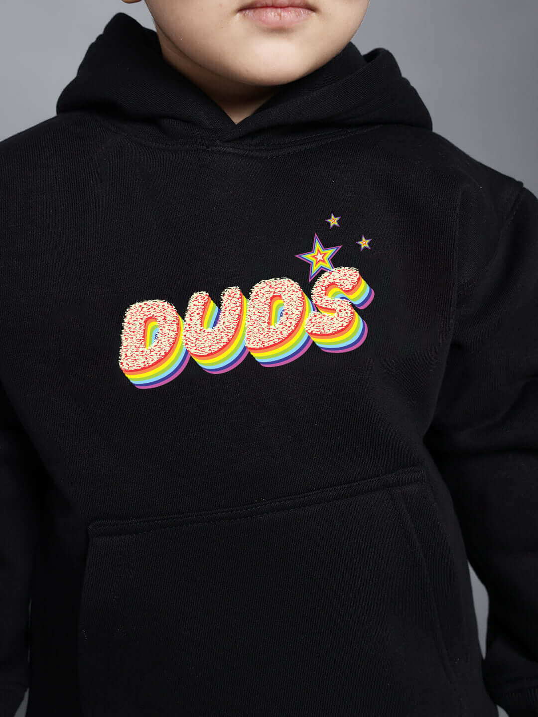 Child wearing black 'DUDS' hoodie with colorful rainbow design and stars.
