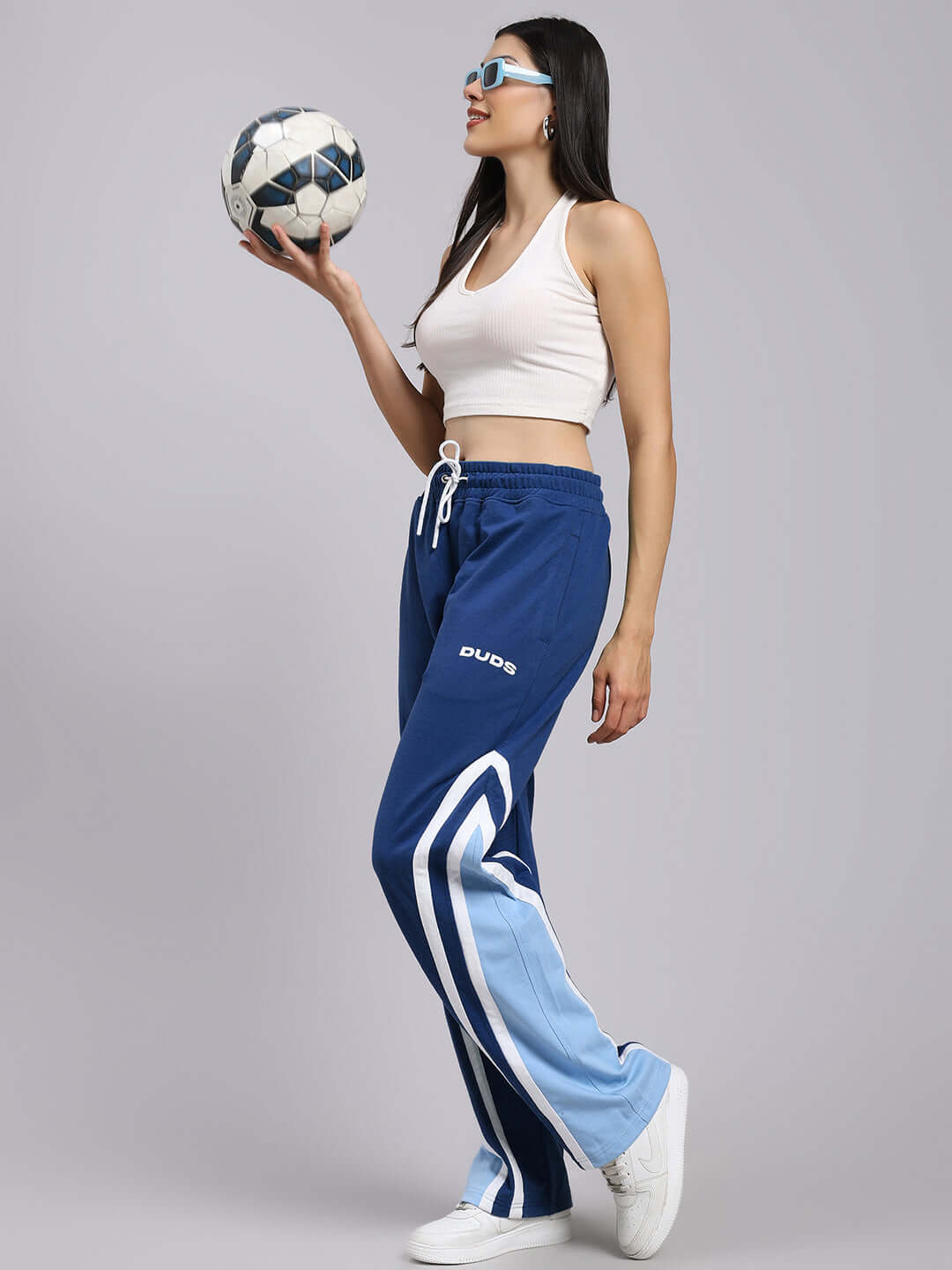 Woman in DUDS blue joggers holding a soccer ball, showcasing relaxed fit and contemporary style.