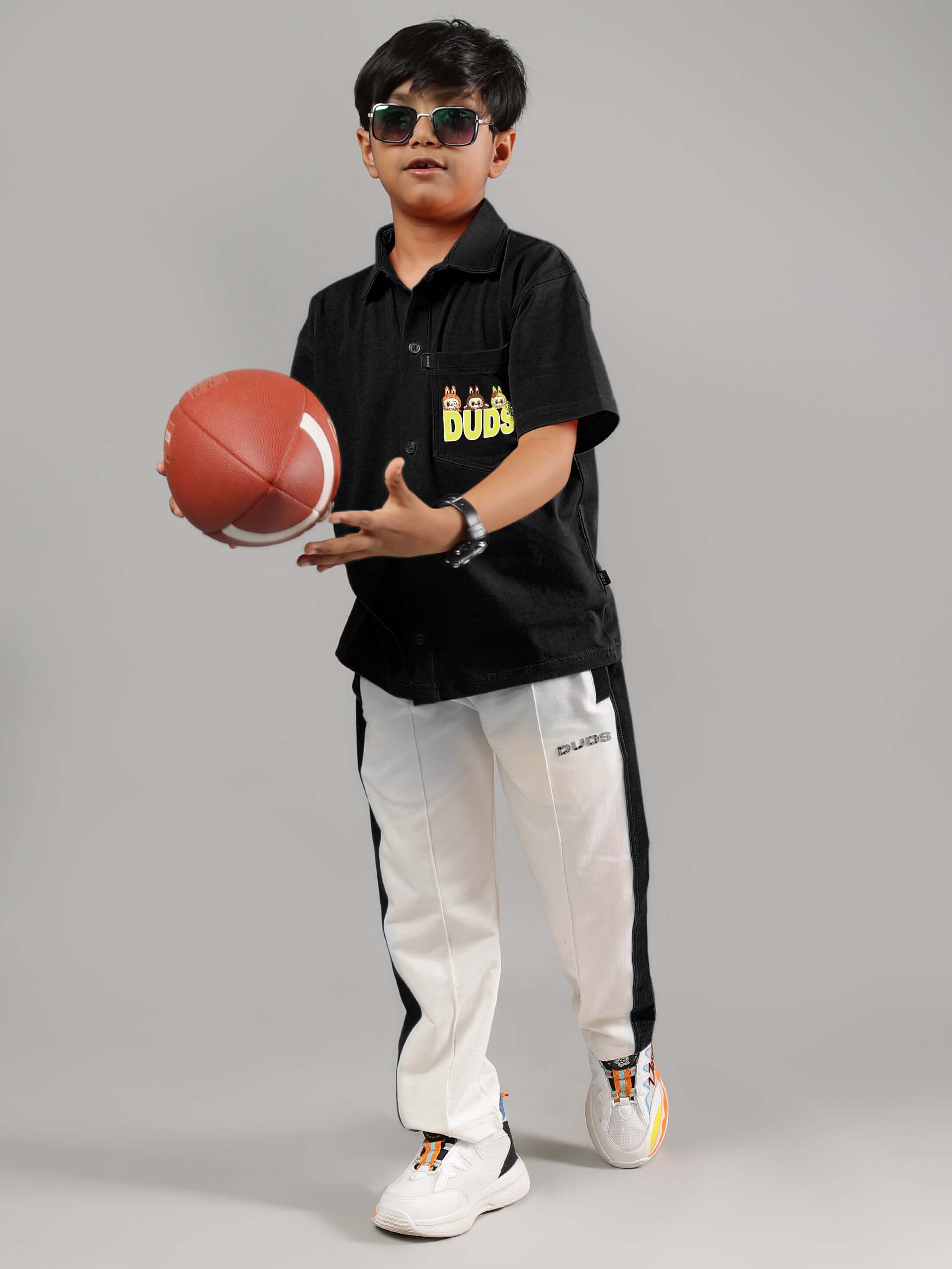 Boy in black and off-white DUDS outfit holding a football, featuring LABUBU design.